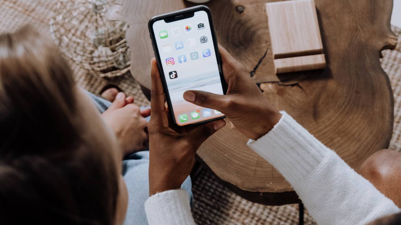 Mulher negra segurando um celular onde se vê o ícone de vários aplicativos