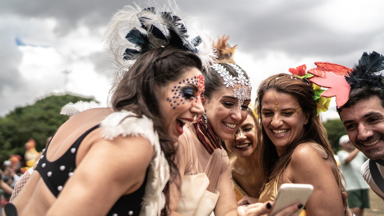 Grupo de amigos usando celular em festa de carnaval de rua