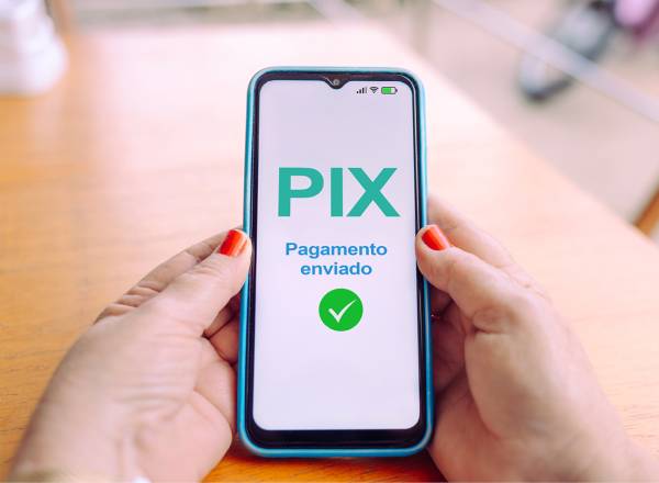 Mãos segurando um smartphone exibindo uma confirmação de pagamento via Pix.