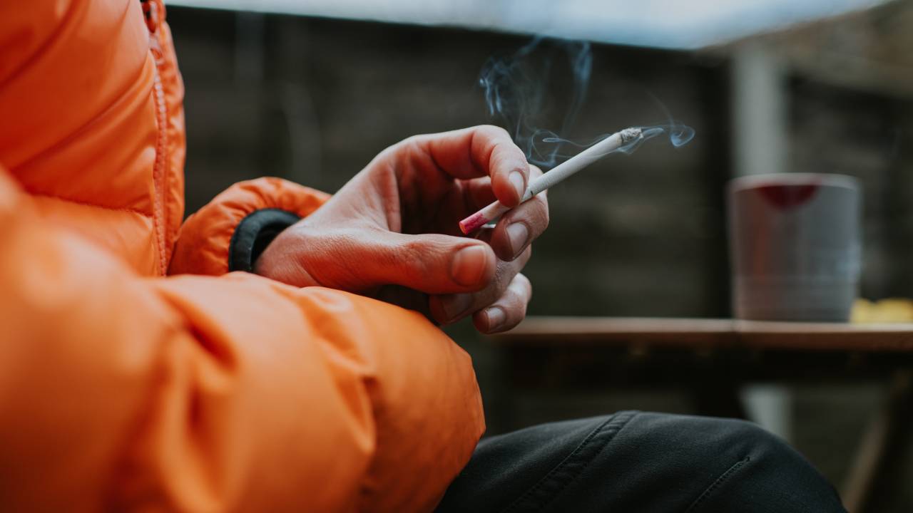 Close-up da mão de um homem segurando um cigarro.