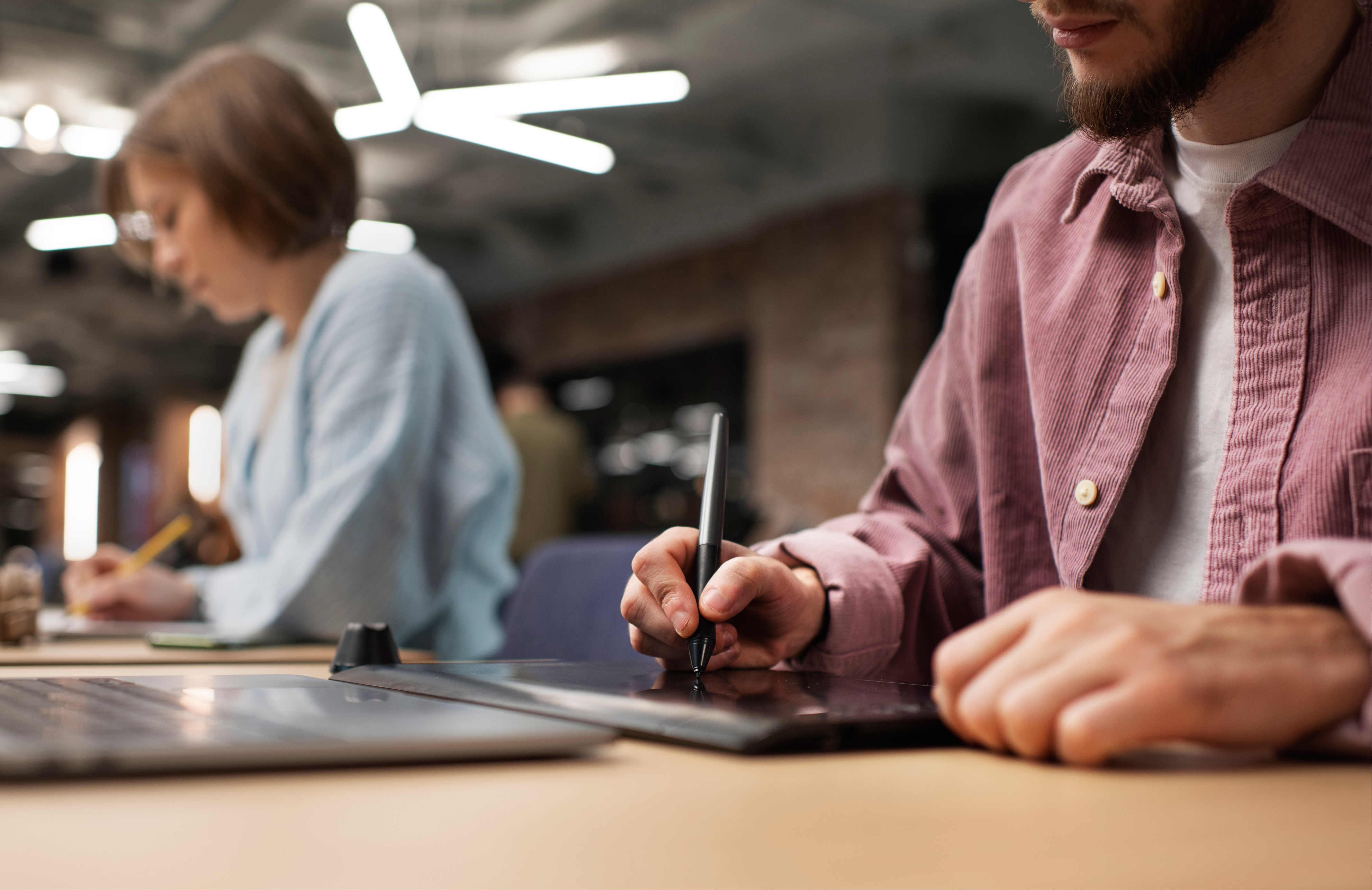 Duas pessoas em uma mesa, com foco em um homem que está escrevendo em uma mesa digitalizadora.